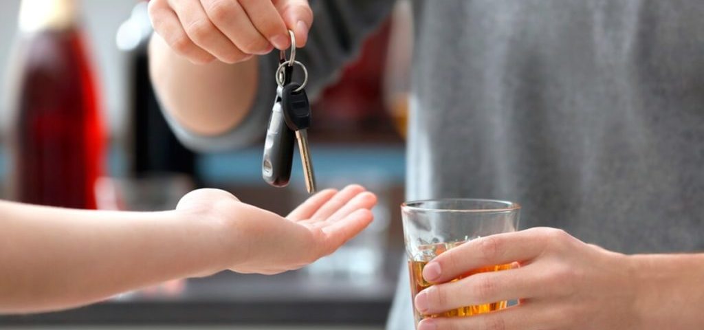 Motorista com copo de cerveja na mão, entregando a chave do veículo para outro condutor.