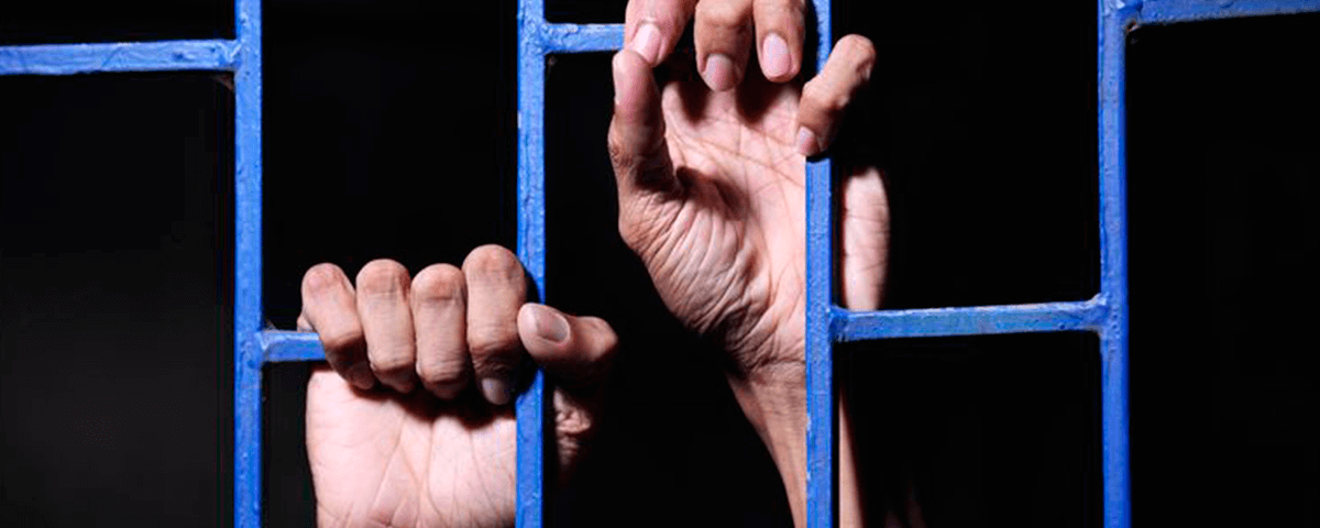 Prisioneiro com as mãos na grade da janela.