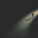 Homem caminhando em pista asfaltada, com iluminação em seu percurso.