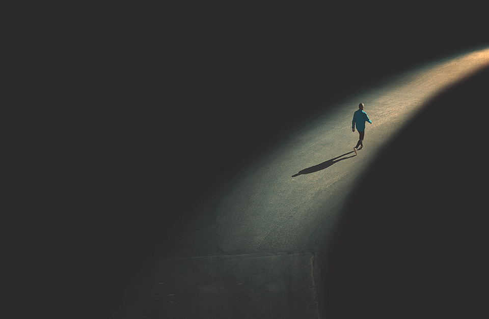 Homem caminhando em pista asfaltada, com iluminação em seu percurso.