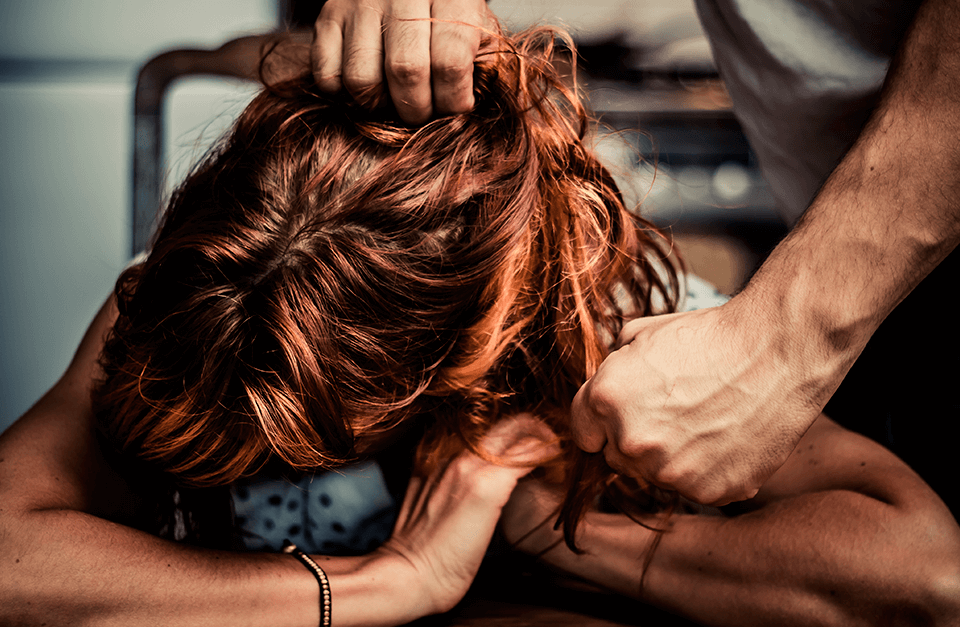Homem puxando cabelo de mulher com a cabeça abaixada.